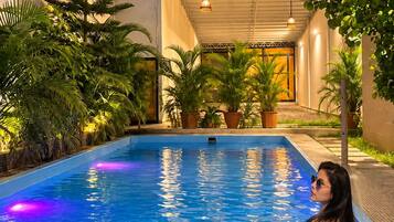 Una piscina con una persona en traje de baño azul, rodeada de macetas y luces colgantes.
