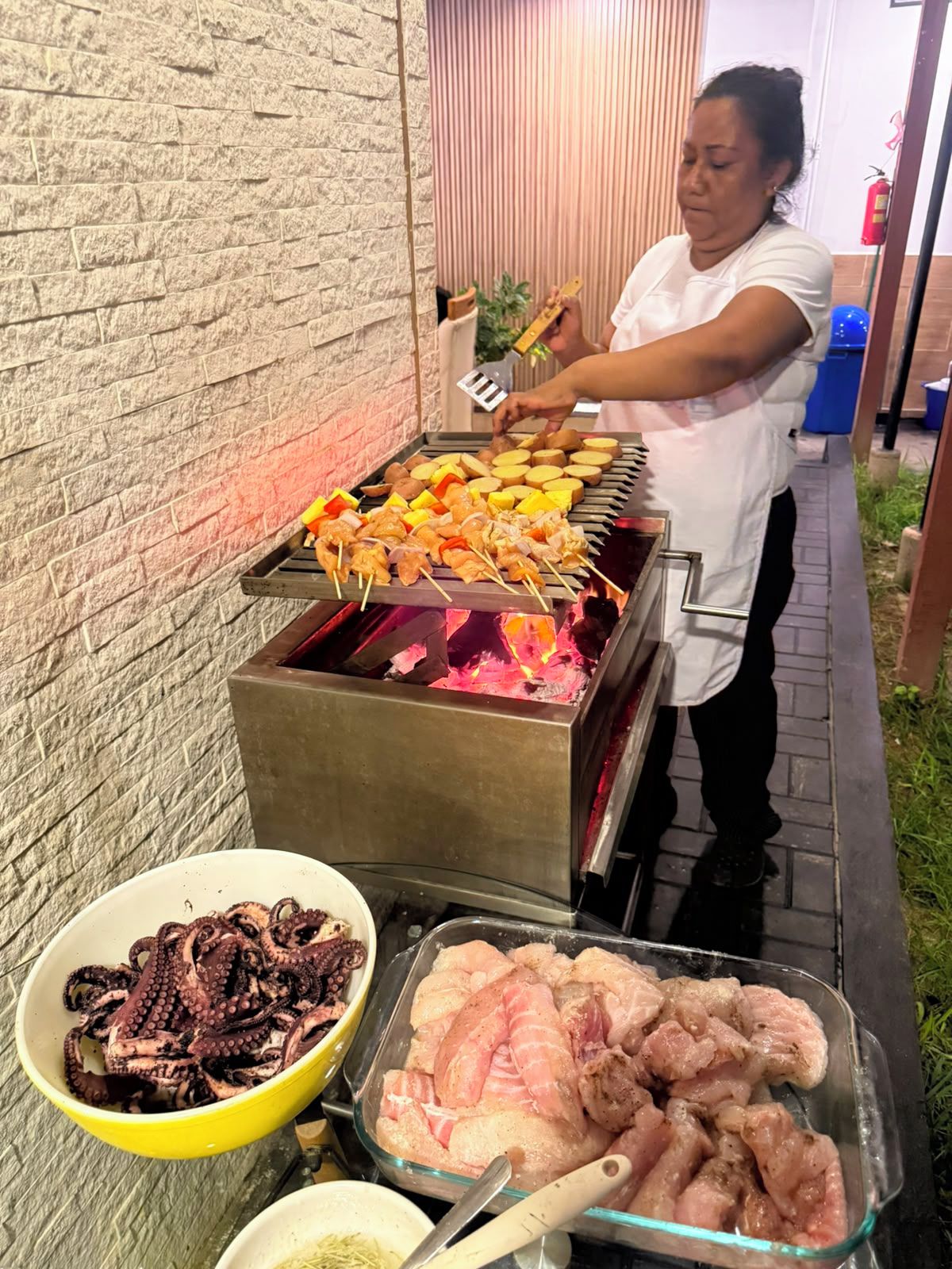 A person grilling various meats and vegetables on an outdoor grill.