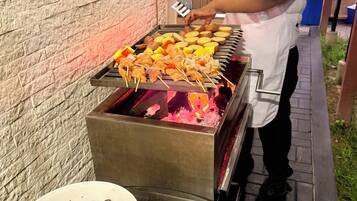 A person grilling various meats and vegetables on an outdoor grill.