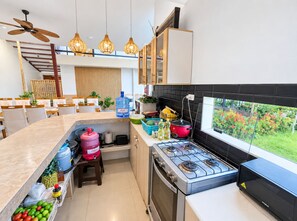 Una cocina moderna con estufa a gas, un dispensador de agua grande y un comedor con ventilador de techo alto.