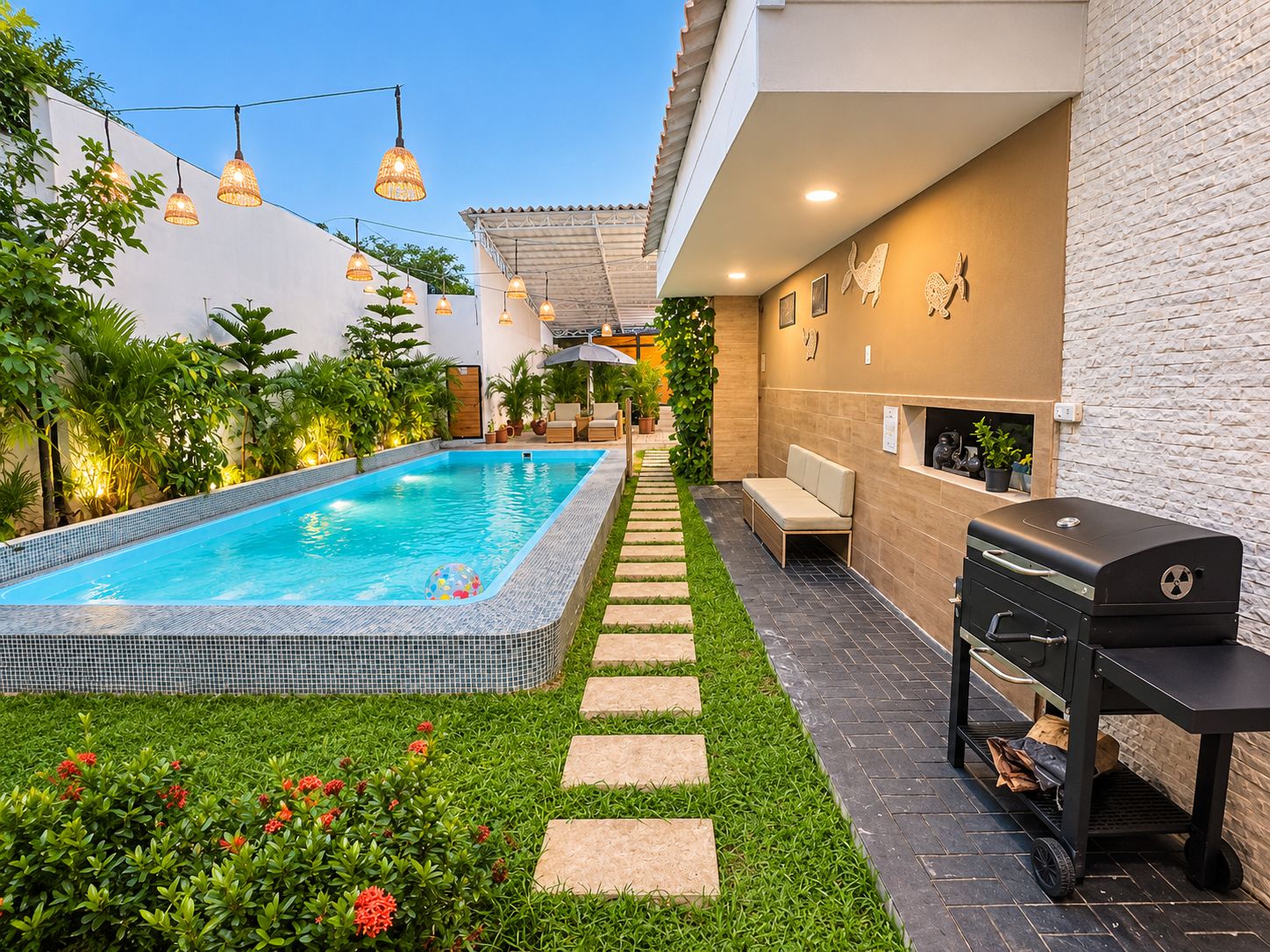 Ein Schwimmbecken mit einer gefliesten Kante, umgeben von einem Garten mit grünem Rasen und roten Blumen. Ein Grill und eine Sitzgelegenheit mit einer Bank sind vorhanden.