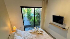 A hotel room with a bed, a TV mounted on the wall, and a view of a garden through a sliding door.