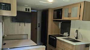 A compact RV kitchen with wooden cabinetry, a built-in microwave, a stove, and a sink.