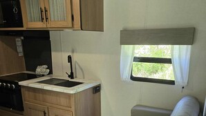 A compact RV kitchen with a stove, sink, and wooden cabinets.