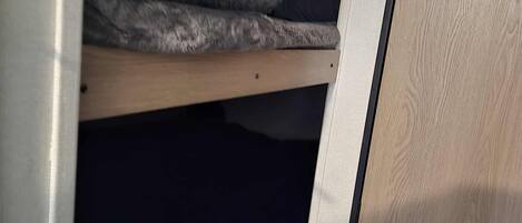 A bunk bed with a window above, a wooden door, and a light-colored wall.