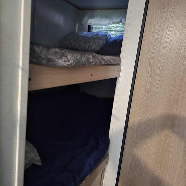 Una cama individual superpuesta con una ventana arriba, una puerta de madera y una pared de color claro.