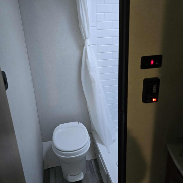 A small, compact bathroom with a white toilet, a white shower curtain, and a wall-mounted flush button. - Back road camper in New Straitsville on monday creek and by old mans cave. (New Straitsville)