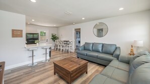 A modern living room with a grey sofa, a wooden coffee table, and a dining area with a white table and chairs. - THE GARDEN HOUSE (Fort Walton Beach)