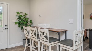 A dining area with a table and four chairs, a potted plant, and a white door. - THE GARDEN HOUSE (Fort Walton Beach)