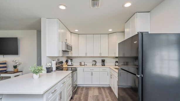 A modern kitchen with white cabinets, a black refrigerator, and a wooden countertop. - THE GARDEN HOUSE (Fort Walton Beach)
