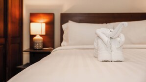 Un lit bien fait, avec une serviette disposée en forme de nœud, une lampe de chevet et une œuvre d’art murale au-dessus du lit.