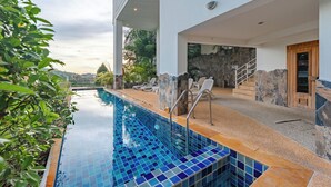 Un espace piscine moderne avec une piscine à l’eau d’un bleu limpide, des murs en pierre et une porte en bois.