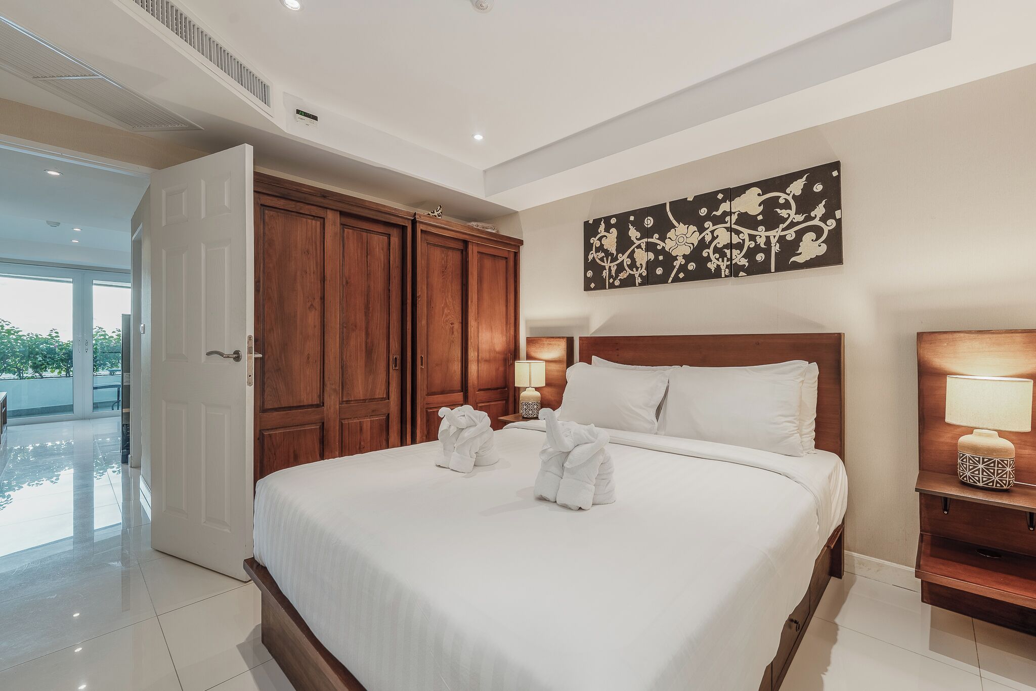 A hotel room with a large bed, wooden wardrobe, and a painting on the wall.