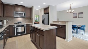 Une cuisine moderne avec des meubles en bois foncé, des appareils en acier inoxydable et un îlot central de couleur claire.