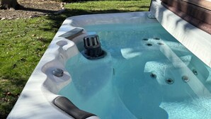 Un bain à remous dans un jardin, avec une pelouse, des arbres et une maison en arrière-plan.