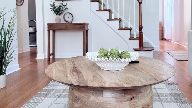 Une table ronde en bois sur laquelle repose un bol blanc, un escalier avec des rampes en bois et un tableau encadré accroché au mur.