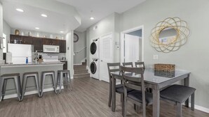 Une cuisine moderne dotée d’un îlot central, de tabourets de bar, d’une table à manger avec des chaises, d’un lave-linge et d’un miroir décoratif.
