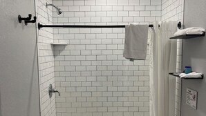 A bathroom with a shower, toilet, and sink, featuring white subway tiles and a black towel rack. - Newly remodeled 14-room hotel in charming St. Mary's . (St. Marys)