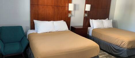 Una habitación de hotel con dos camas, un sillón color turquesa, cabeceros de madera y lámparas de noche.