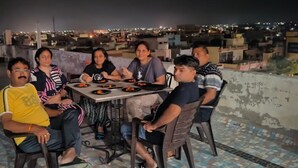 Un groupe de personnes est assis autour d’une table sur une terrasse en toit, avec une vue sur la ville en arrière-plan.