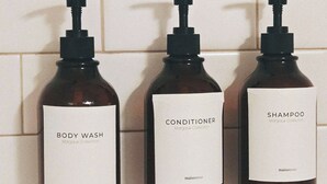 Drei Flaschen Duschgel, Conditioner und Shampoo aus der Margaux Kollektion, angeordnet an einer gefliesten Wand.