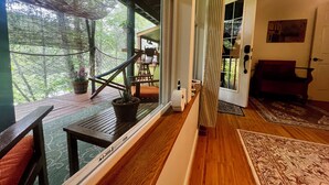 A room with a wooden floor, a potted plant, a chair, a bench, and a door leading outside. - unique 1-bedroom apt  Organic Farm&Resort in Murphy with AC (Murphy)