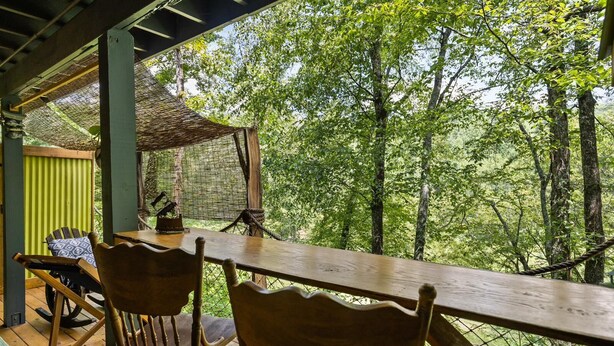 An outdoor wooden deck with two chairs and a table, surrounded by a wire mesh fence and trees. - unique 1-bedroom apt  Organic Farm&Resort in Murphy with AC (Murphy)