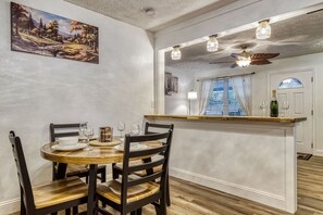 A dining area with a round wooden table, four chairs, and a bar counter with a bottle of champagne.