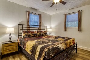 A bedroom with a bed, two bedside tables, a ceiling fan, and two windows with curtains.