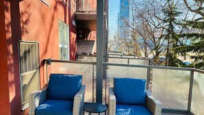 Parvekkeella on rottinkituoleja ja pieni pöytä, ja sieltä avautuu näkymä kaupunkimaisemaan ja puustoon.