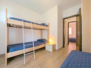 Une chambre avec un lit superposé, une échelle, une table de chevet avec une lampe et une porte donnant sur une autre pièce.