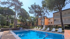 A swimming pool with tiled edges, surrounded by lounge chairs and trees.