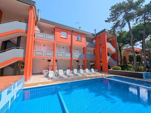 Un immeuble à plusieurs étages doté d’une piscine, d’un espace extérieur aménagé et offrant une vue sur un ciel dégagé.