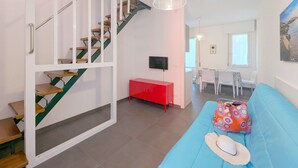 A modern living room with a staircase, a dining area, and a sofa with a colorful bag.