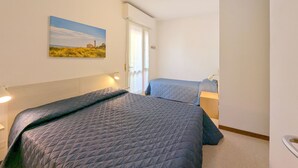 Un dormitorio con dos camas, un cuadro de un paisaje, una lámpara de techo y una puerta.