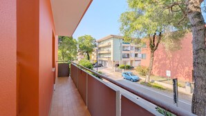 Un balcón con vista a una calle residencial, un coche estacionado y un árbol.