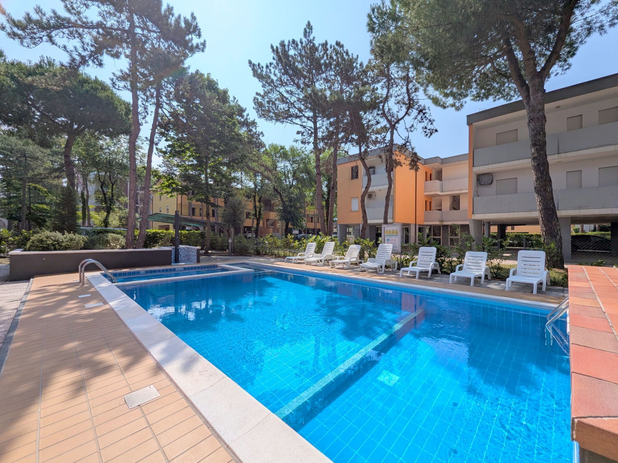 Une piscine dont les bords sont recouverts de carreaux, entourée de chaises longues et d’arbres.