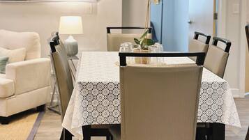 A dining area with a table set for four, surrounded by chairs, a lamp, and a vase with flowers.