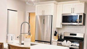 A modern kitchen with white cabinets, stainless steel appliances, and a wooden dining table with chairs. - Downtown 5BR Home for 10 Guests with Kitchen & W/D (Providence)