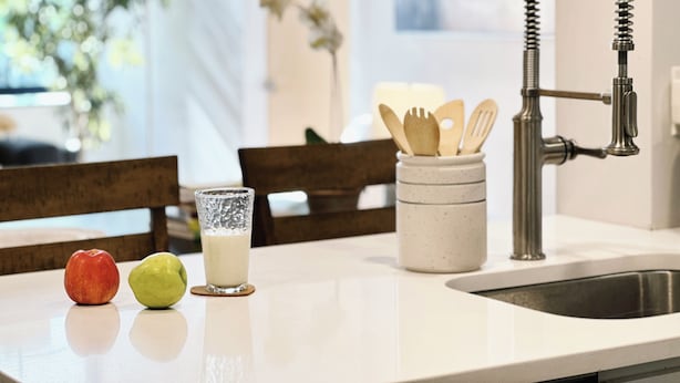 A kitchen counter with a stainless steel faucet, a glass of milk, and a container of wooden utensils. - Downtown 5BR Home for 10 Guests with Kitchen & W/D (Providence)