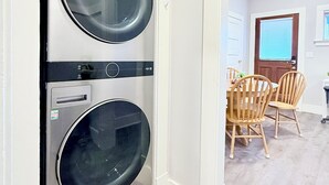 A laundry room with two front-loading LG washers and dryers, a dining area with a wooden table and chairs, and a door leading to another room. - Light filled apt in Historic Home by UW & Downtown (Seattle)