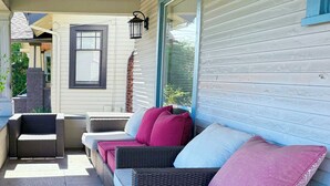 A covered outdoor seating area with wicker furniture and cushions, a window with blinds, and a brick chimney. - Light filled apt in Historic Home by UW & Downtown (Seattle)