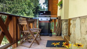 Une terrasse extérieure en bois, équipée d’un barbecue, d’une table et de chaises.
