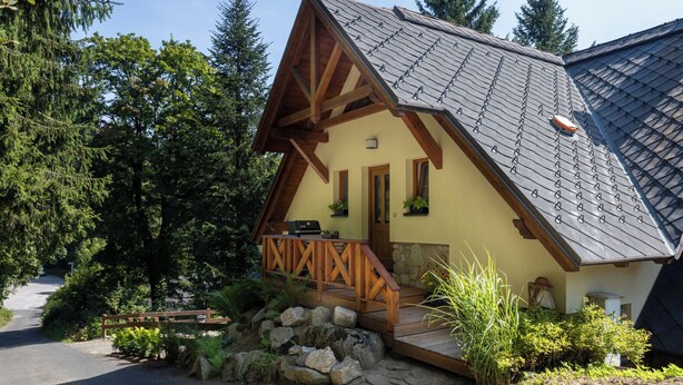 Une cabane avec un toit en pente, une véranda en bois et des fondations en pierre.
