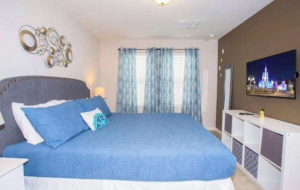 A bedroom with a bed, curtains, a television, and wall decor.