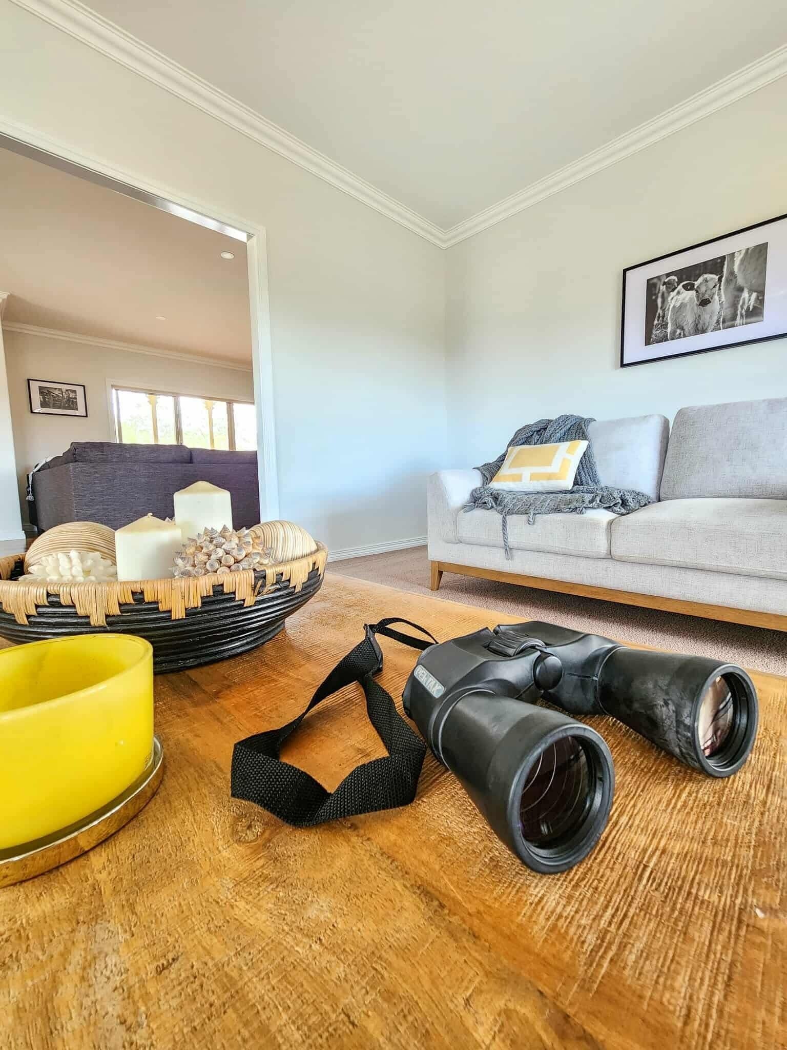 Ein Wohnzimmer mit einer Couch, einem gerahmten Bild, einem Korb mit Kerzen und einem Fernglas auf dem Boden.