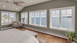 Une chambre avec de grandes fenêtres, un ventilateur de plafond et un télescope monté sur un trépied.
