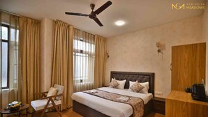 Quarto de hotel com uma cama grande, um ventilador de teto, uma escrivaninha com cafeteira e uma cadeira.