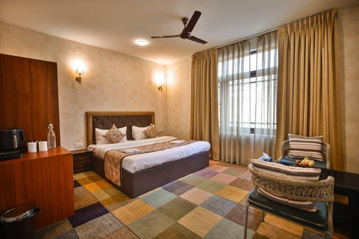A hotel room with a bed, a desk, a chair, a ceiling fan, and a window with curtains.