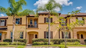 A multi-story residential building with balconies, a brick pathway, and palm trees.